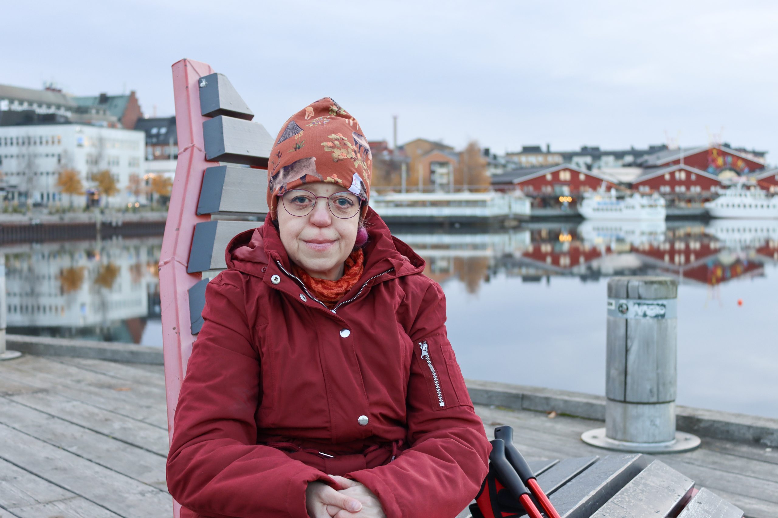 Eva Uvemalm sitter på en stol vid vattnet i Luleå. Bakom syns byggnader. Foto: Elin Westerlund